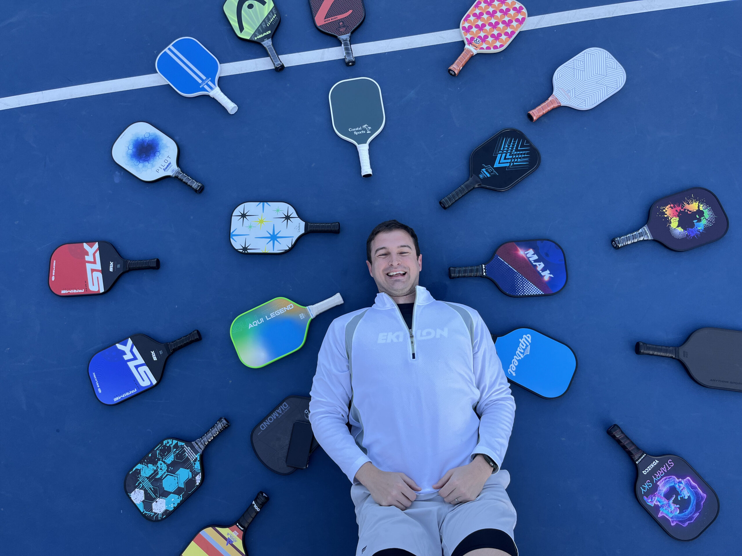 Picture of man surrounded by beginner pickleball paddles.