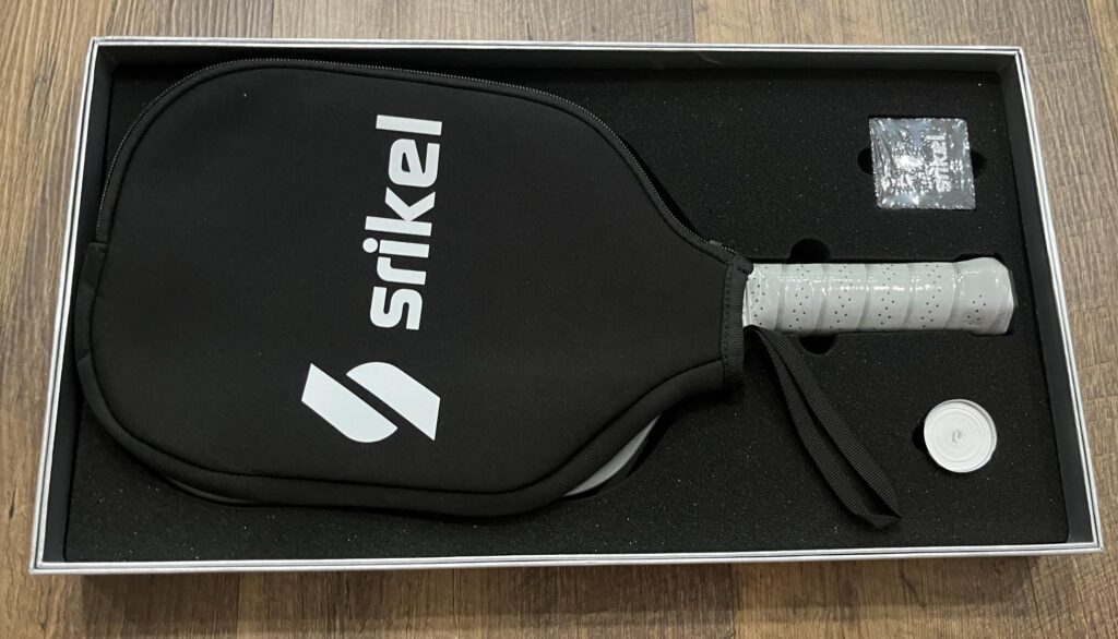Picture of the open Srikel pickleball paddle box showing the paddle, cover, carbon eraser and grip tape.
